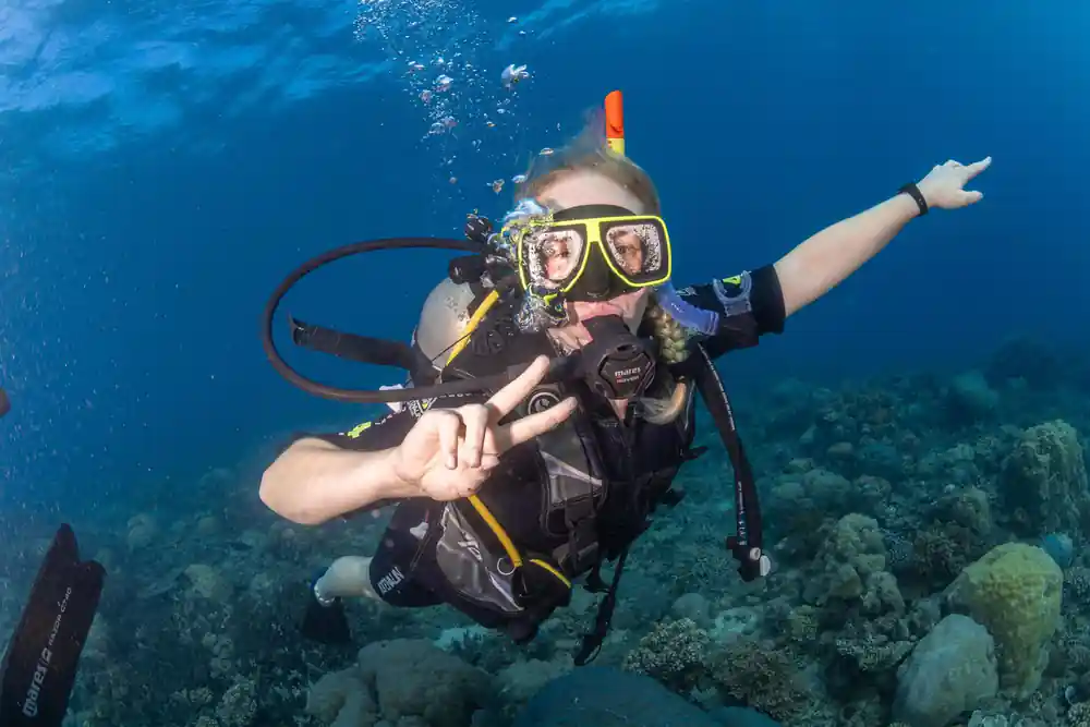 A diver making a peace sign above a shallow coral garden