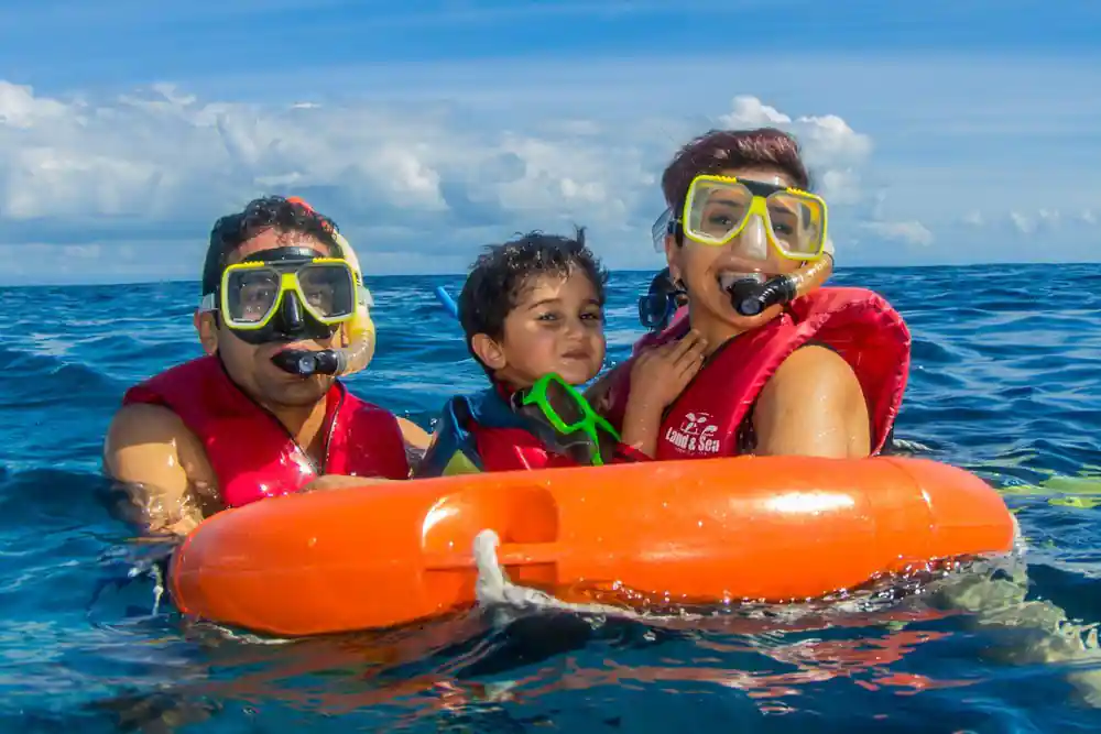 Two adults and a child holding an orange flotation ring at the surface