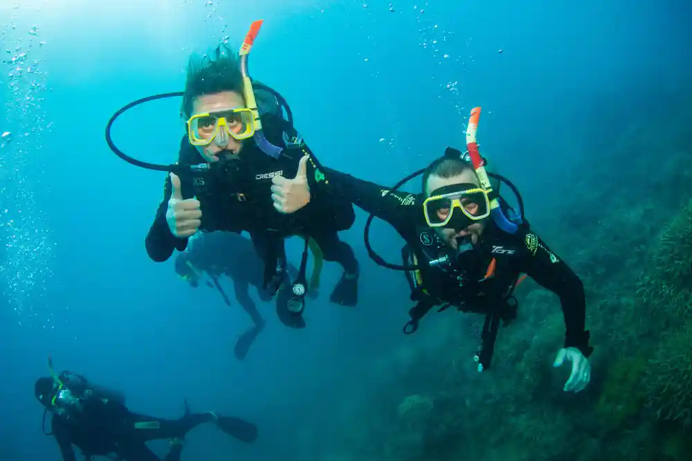 Two divers giving thumbs up side by side over the coral